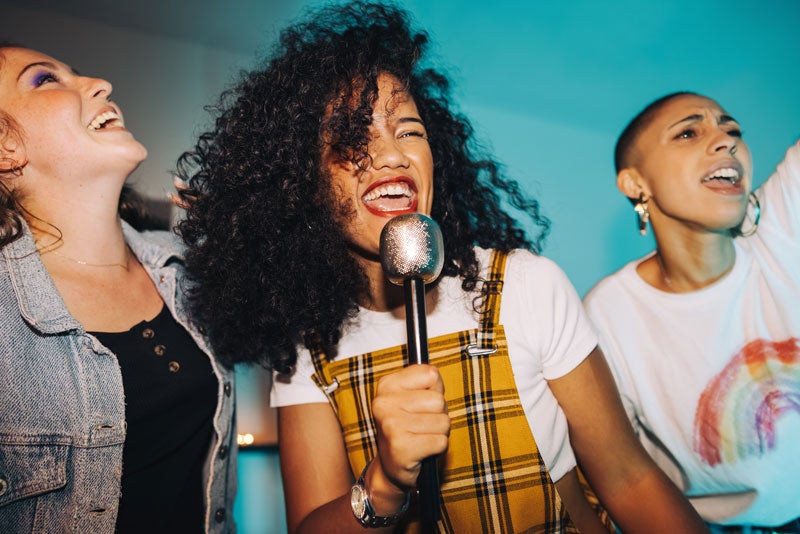 Grupo de três amigas aproveitando o momento de receber visita em casa para cantar no karaokê